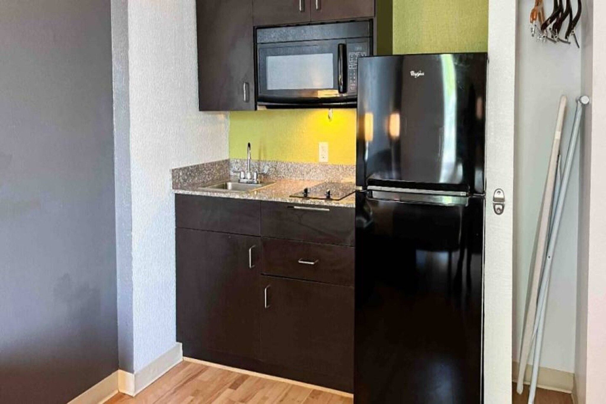 Una cocina pequeña con muebles oscuros, un microondas y un refrigerador negro.