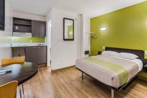 Una camera d'albergo con un letto, una scrivania, una sedia, uno specchio e un angolo cottura.