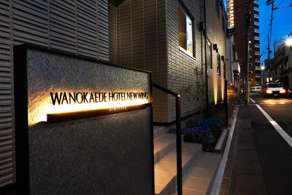 Un letrero de hotel con el nombre 'WANOKAEDE HOTEL NEWWING' iluminado durante la noche.