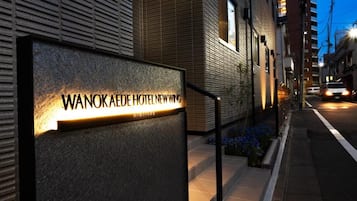 Un letrero de hotel con el nombre 'WANOKAEDE HOTEL NEWWING' iluminado durante la noche.