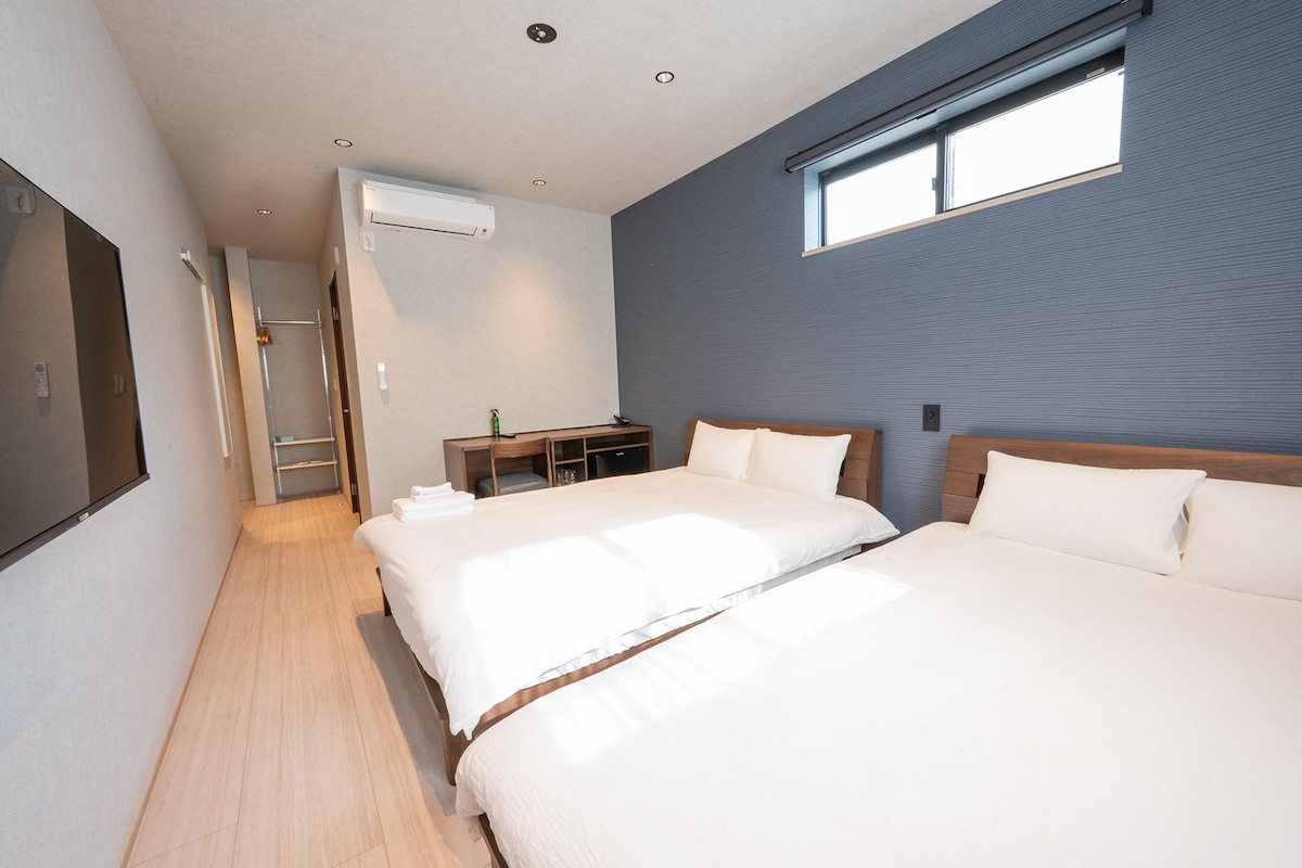 A hotel room with two beds, a desk, a chair, an air conditioning unit, and a window.