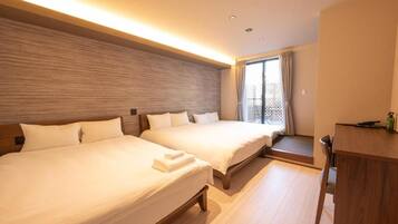 Habitación de hotel con dos camas, cabecero de madera, ventana con cortinas y un pequeño escritorio con una silla.