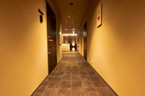 A hotel hallway with a tiled floor, doors on both sides, and a wall-mounted light fixture.