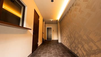 A hallway with a wooden door, a wall-mounted light fixture, and a patterned wall.