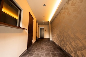 A hallway with a wooden door, a wall-mounted light fixture, and a patterned wall.