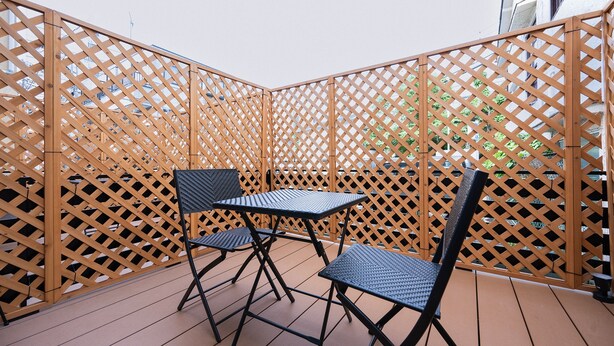 A wooden deck with a lattice fence, two chairs, and a table. - WANOKAEDE HOTEL NEW WING (Tokyo)