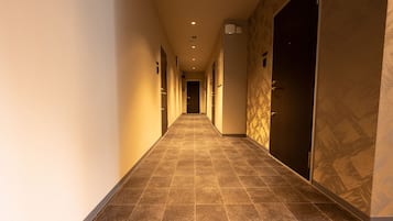Un pasillo de hotel con suelo de baldosas, puertas a ambos lados e iluminación empotrada.