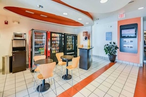 Een modern interieur met automaten, een kleine koelkast en een zithoek met tafels en stoelen.