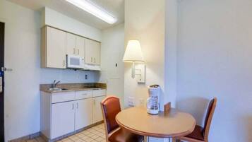 A compact kitchen with white cabinets, a microwave, a coffee maker, and a table with two chairs.