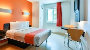 Una camera d'albergo con un letto, un comodino, una sedia e una TV a muro.