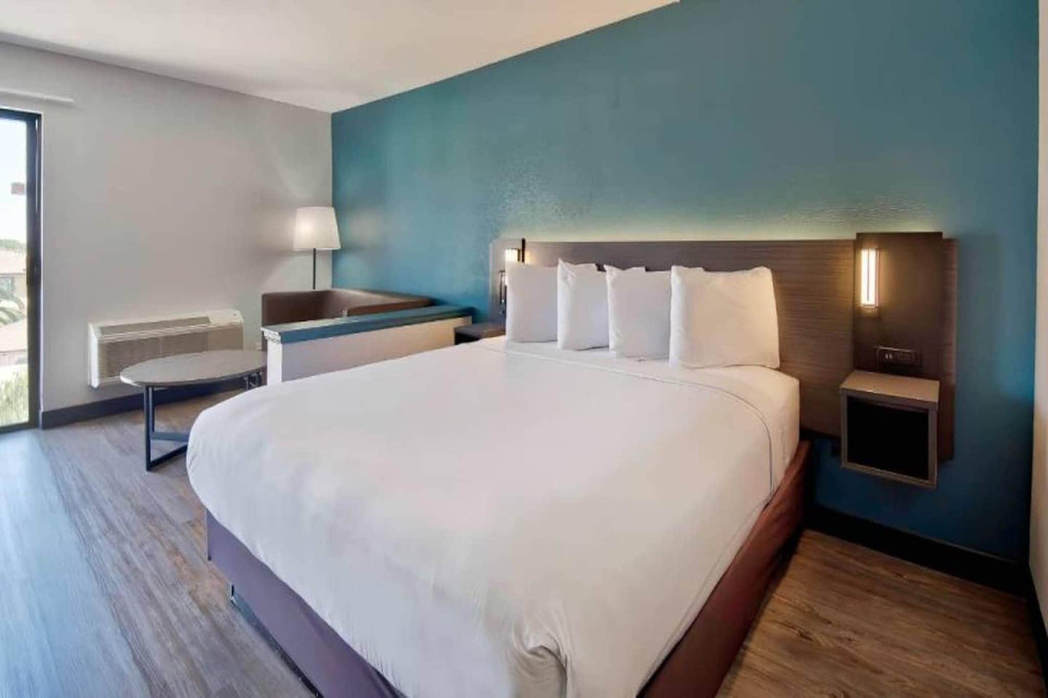 Ein modernes Hotelzimmer mit einem großen Bett, einem Nachttisch, einer Lampe und Blick ins Freie.