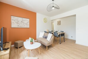 A modern living room with a map, a dining area with chairs and a table, and a television on a stand.