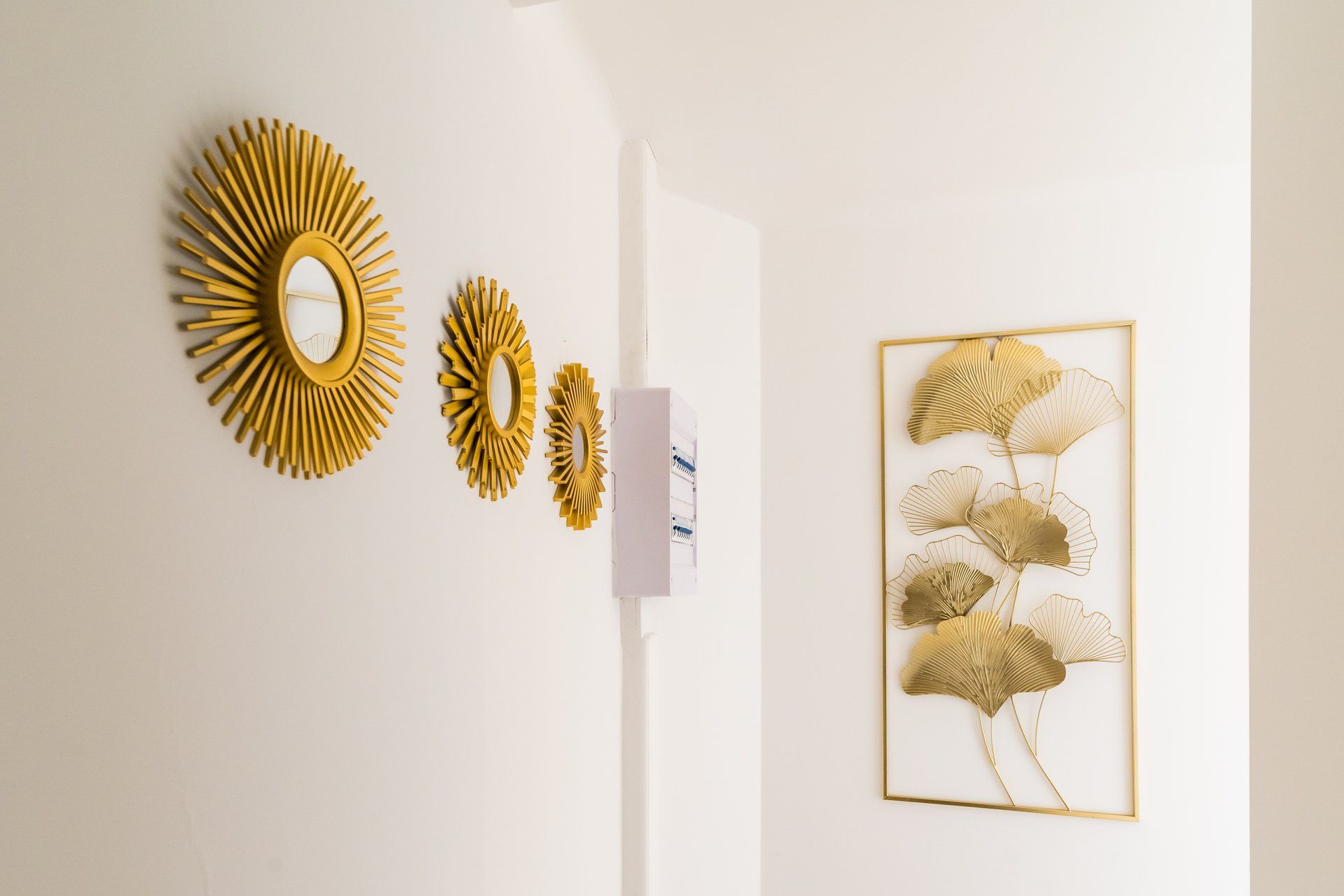 A wall with three golden sunburst mirrors and a framed artwork of golden leaves.