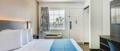 A hotel room with a bed, a desk, a chair, a window with curtains, and a door.