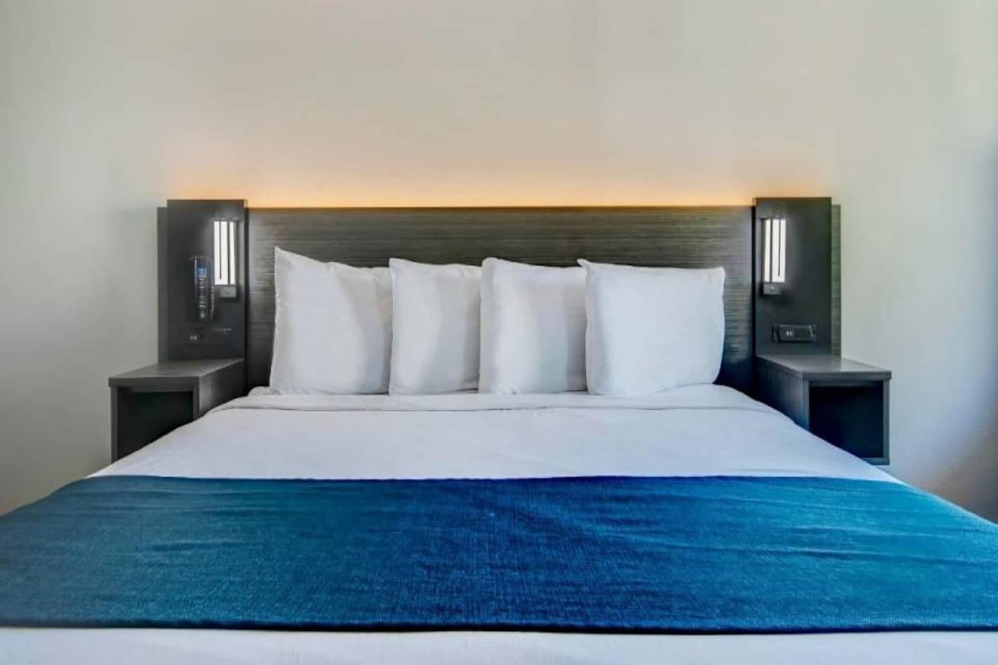 Un lit avec une tête de lit blanche, quatre oreillers blancs et un plaid bleu.