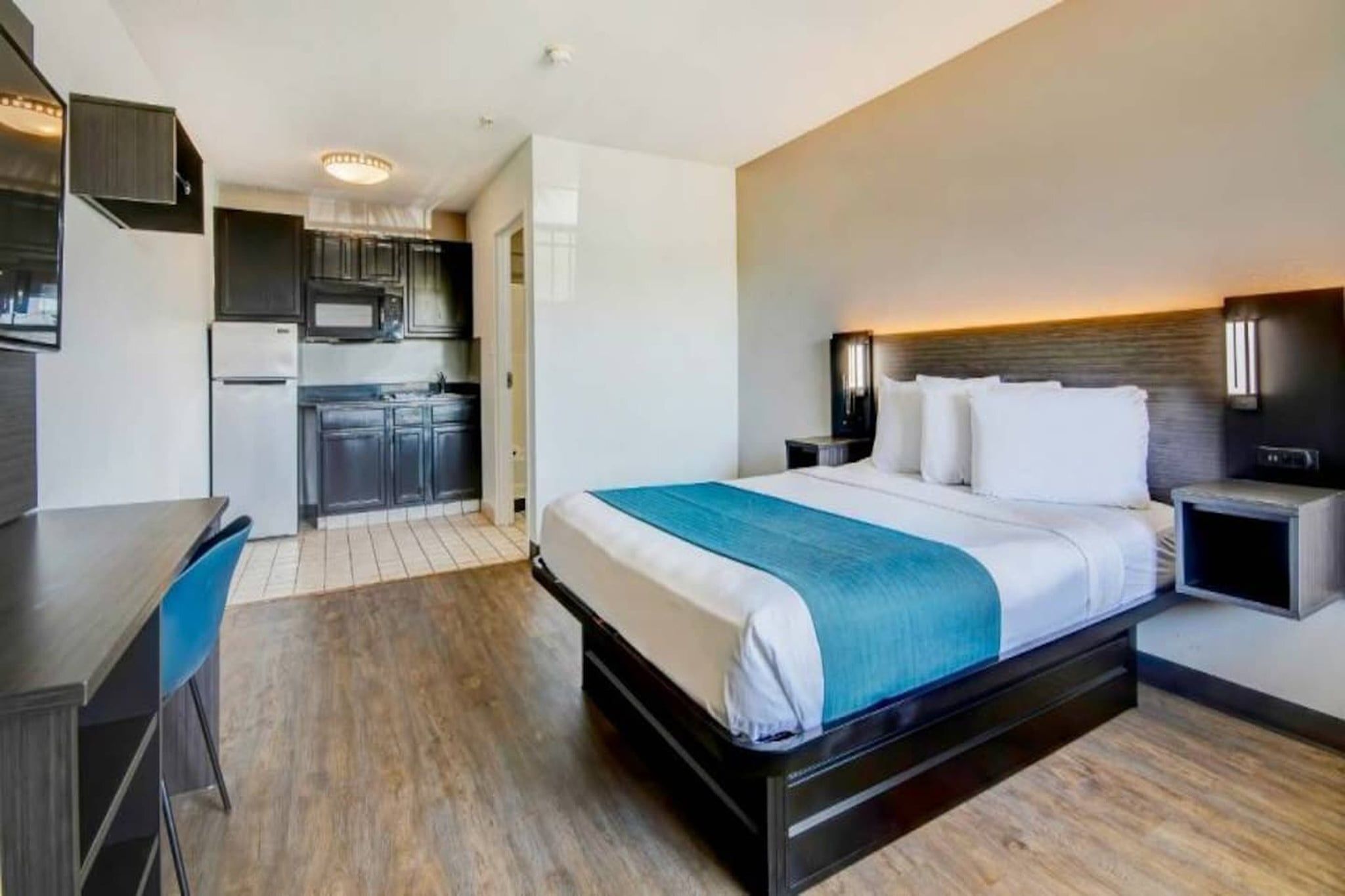 Una habitación de hotel con cama, mesitas de noche, escritorio y kitchenette.