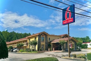 Un motel avec un toit rouge et une façade en pierre, un parking et un ciel d’un bleu éclatant.