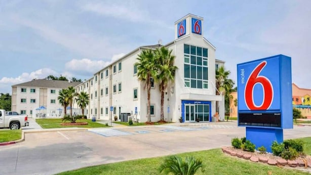 Un motel con un grande cartello con il numero '6', un parcheggio e un edificio con diverse finestre e palme.