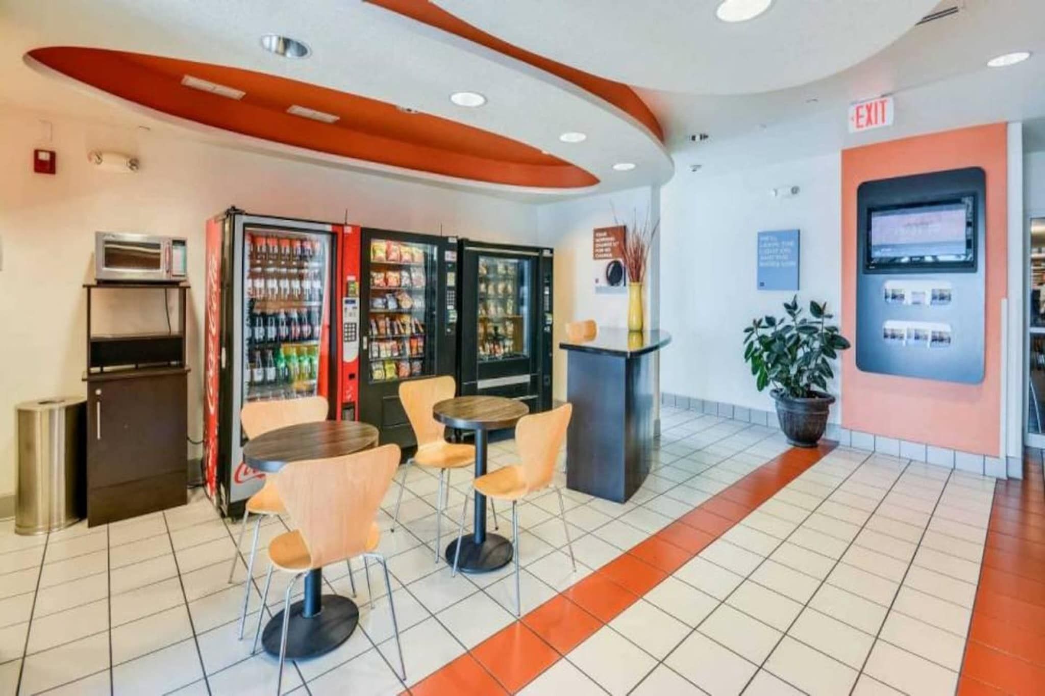 Un intérieur moderne doté de distributeurs automatiques, d’un petit réfrigérateur et d’un espace détente avec des tables et des chaises.