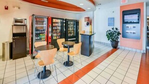 Un interno moderno con distributori automatici, un piccolo frigorifero e un'area salotto con tavoli e sedie.