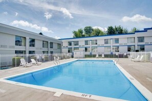 Ein Schwimmbecken mit Liegestühlen und ein Gebäude mit vielen Fenstern im Hintergrund.