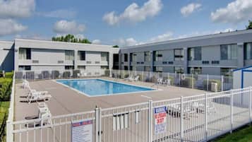 A hotel with a swimming pool surrounded by lounge chairs and a fenced area.