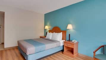 A hotel room with a bed, bedside tables, a chair, and a blue wall.