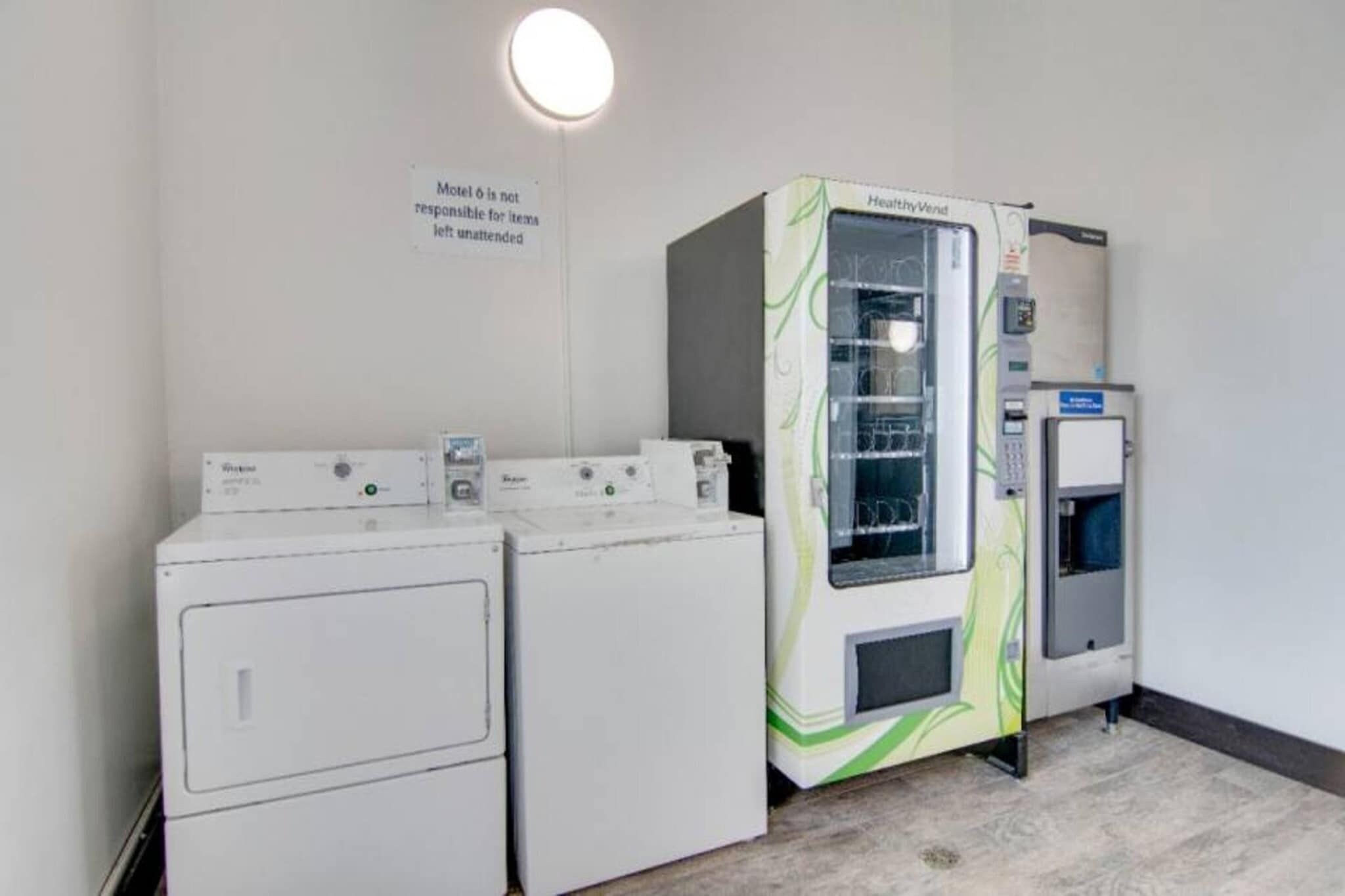 Un área de lavandería con dos lavadoras blancas y una máquina de lavandería autoservicio HealthyVend.