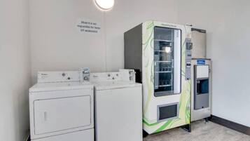 Un área de lavandería con dos lavadoras blancas y una máquina de lavandería autoservicio HealthyVend.