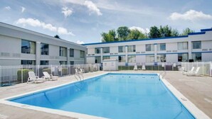 A swimming pool with a white fence, lounge chairs, and a building with multiple windows in the background.