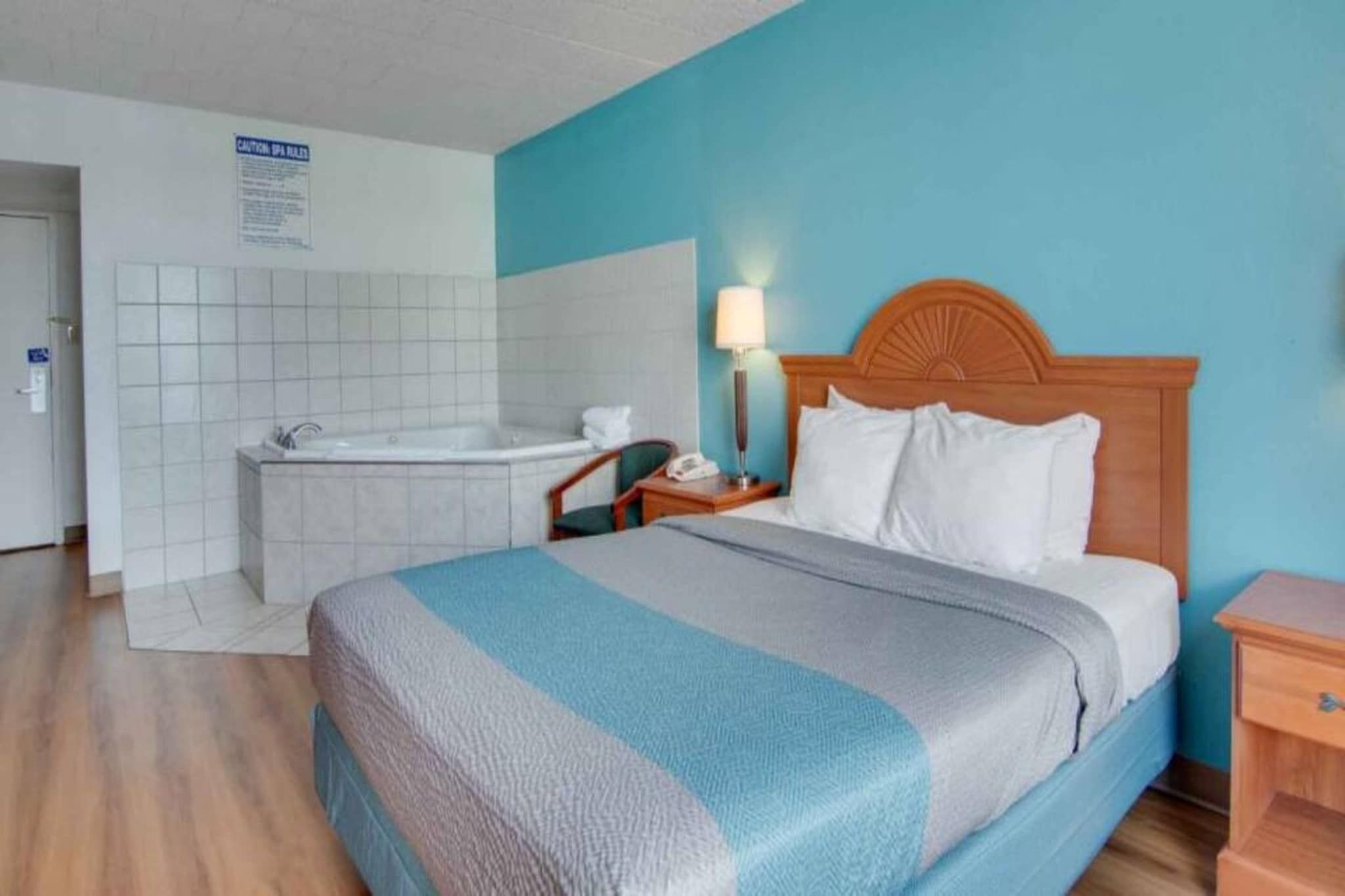 Quarto de hotel com cama, mesa de cabeceira, abajur, banheiro com banheira e uma placa na parede.