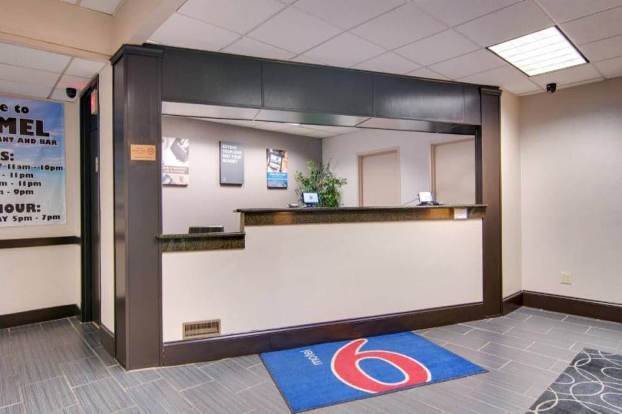A reception area with a counter, a blue mat with a red logo, and a sign indicating the restaurant's hours.