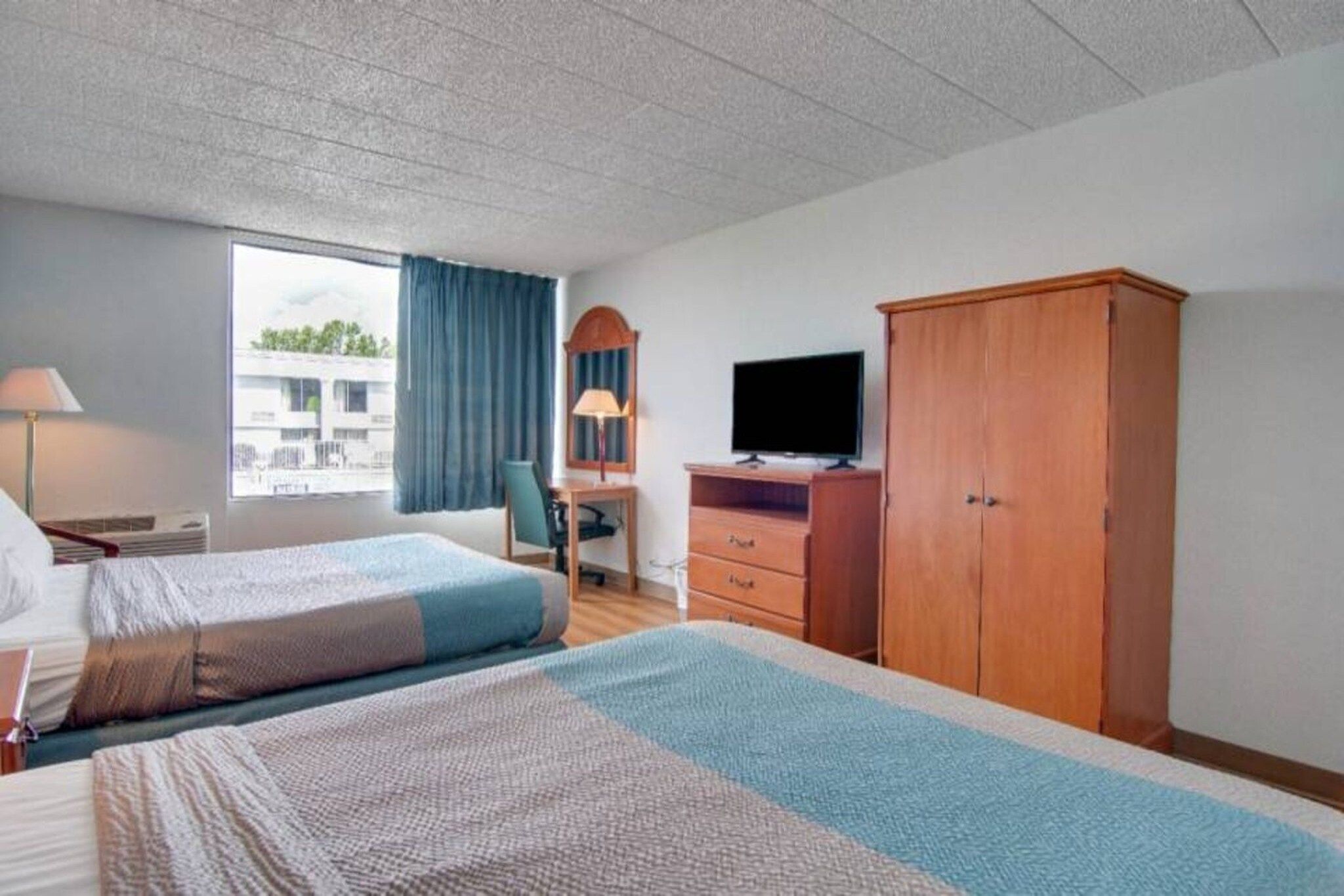 Habitación de hotel con dos camas, un escritorio, un televisor y un armario.