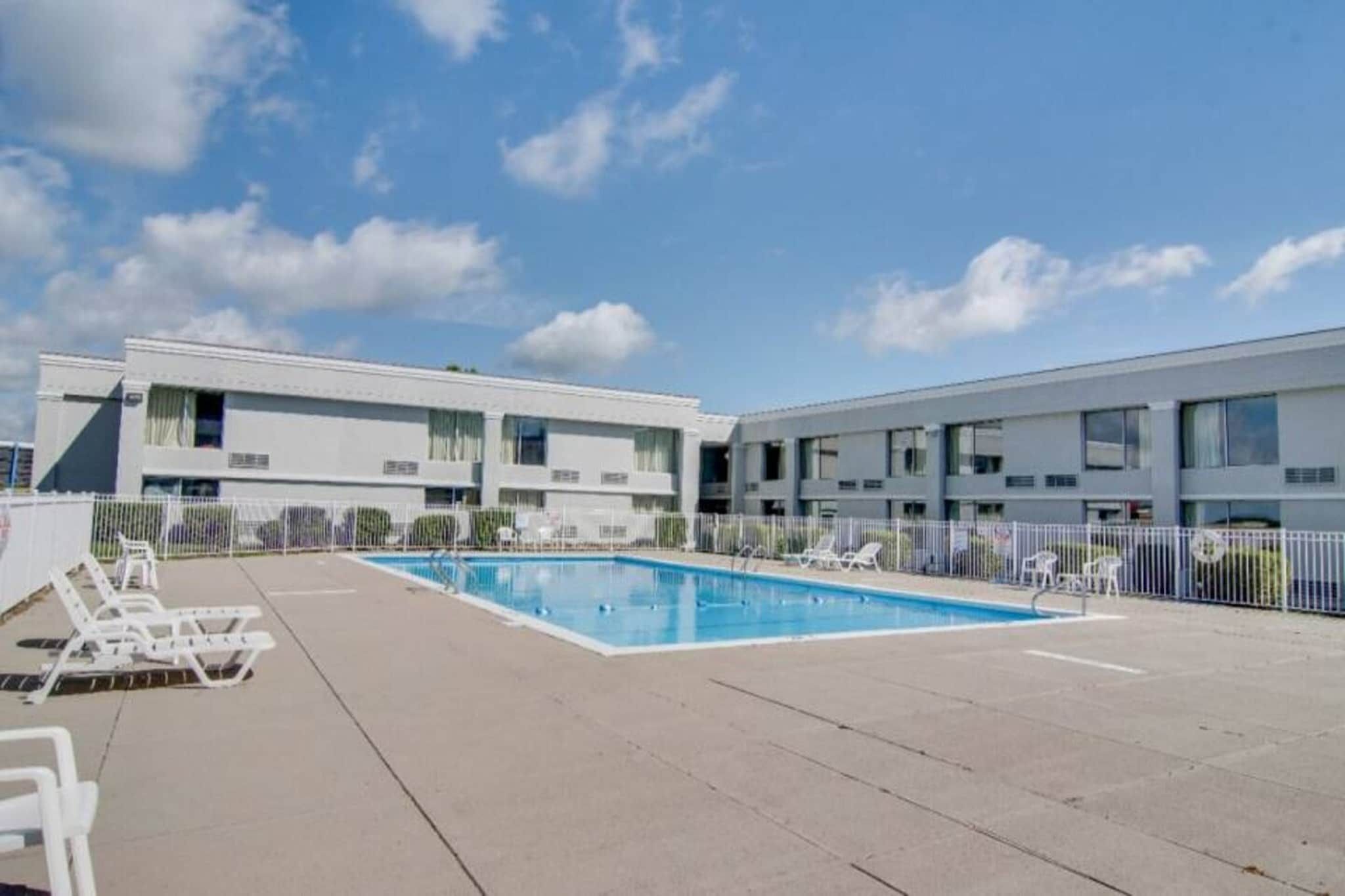 Un hotel moderno con piscina, varios balcones y cielo despejado.
