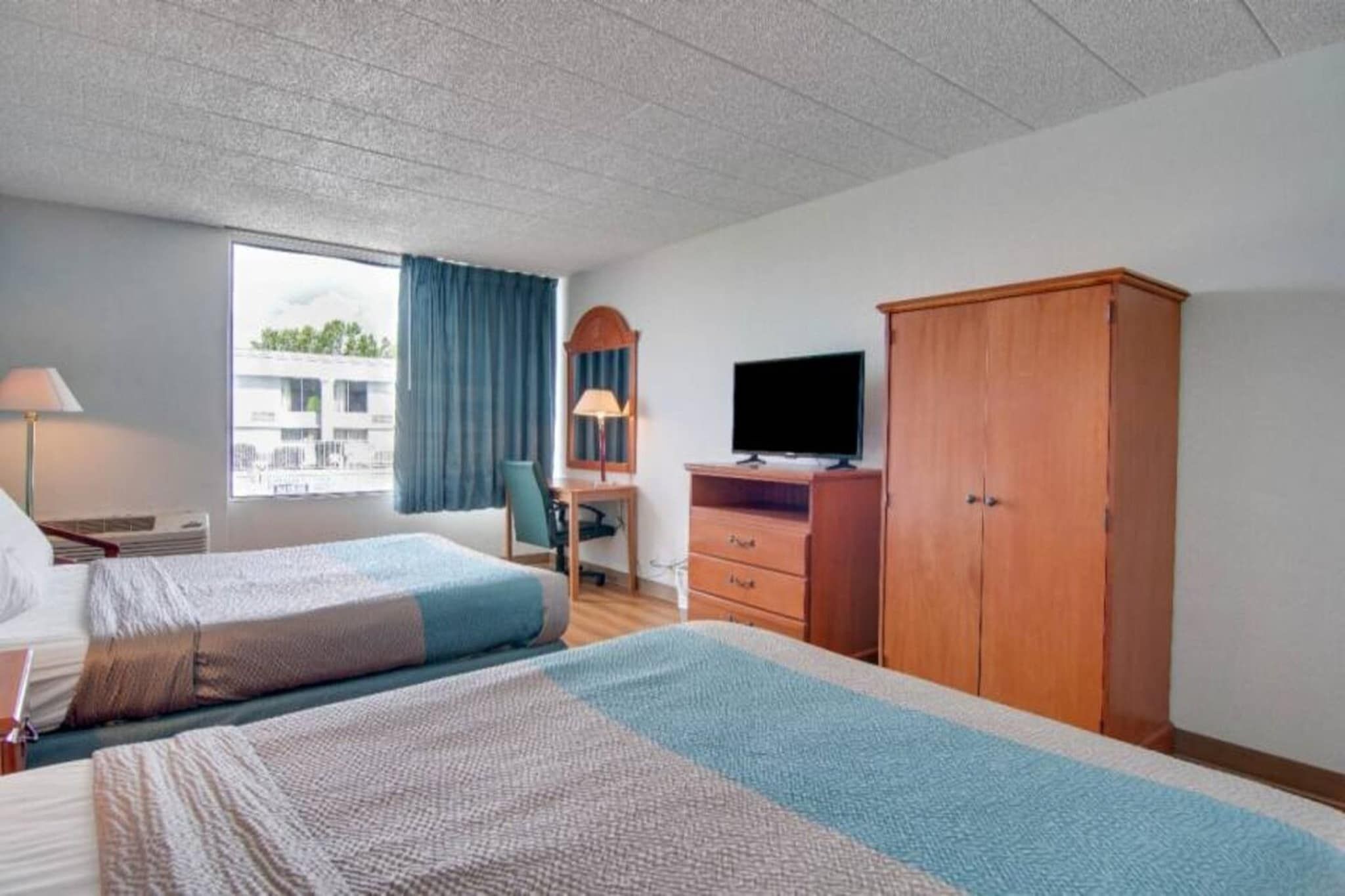 Una habitación de hotel con dos camas, un escritorio con computadora, televisor y armario.