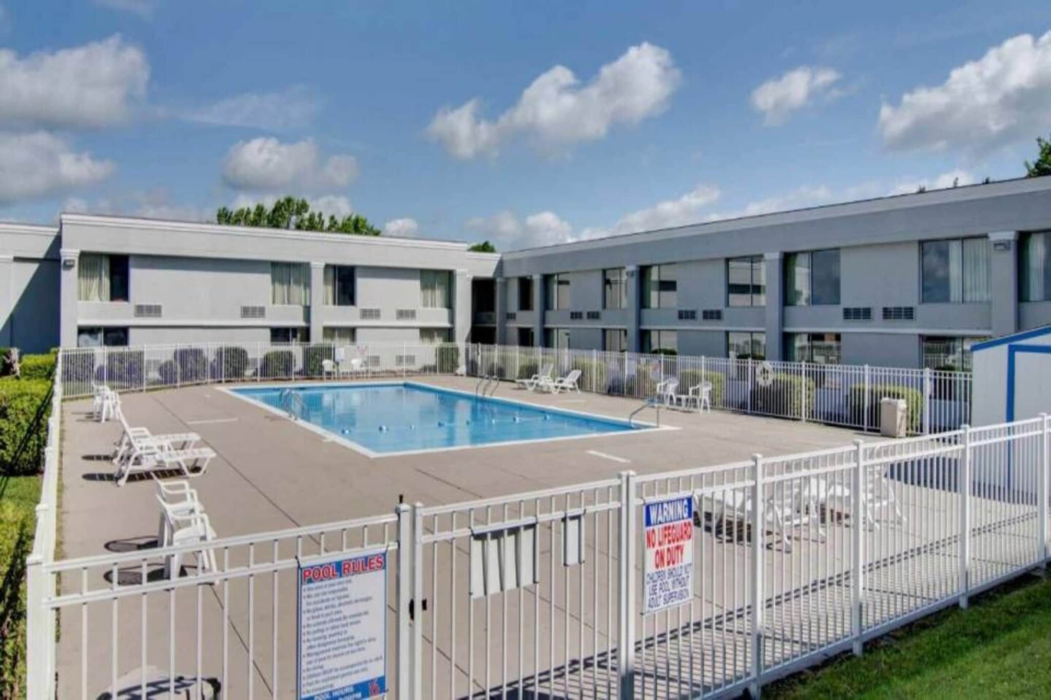 A hotel with a swimming pool surrounded by lounge chairs and a fenced area.