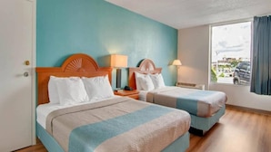 Una habitació d'hotel amb dos llits, ambres de fusta, una finestra amb vista i una porta.