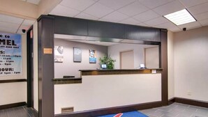 A hotel reception area with a reception desk, a blue carpet with a logo, and a signboard with operating hours.