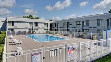 Una piscina con sillones de descanso, un área cercada y un edificio con varias ventanas.