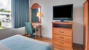 A hotel room with a bed, a desk with a chair, a television, and a wardrobe.