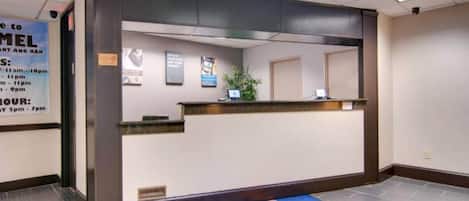 Ein Hotel-Empfangsbereich mit einer Rezeption, einem blauen Teppich mit Logo und einem Schild mit Öffnungszeiten.
