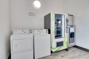 Pesutila, jossa on kaksi valkoista pesukonetta ja yksi HealthyVend-automaattipesukone.