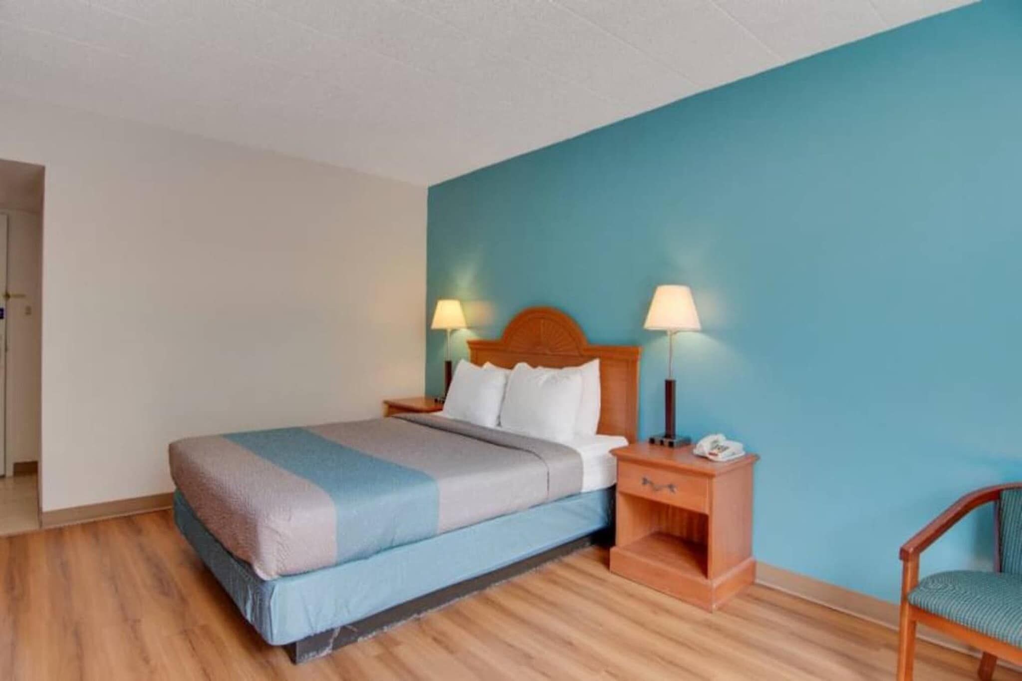 Una habitación de hotel con cama, lámparas de noche, mesita de noche y una silla.
