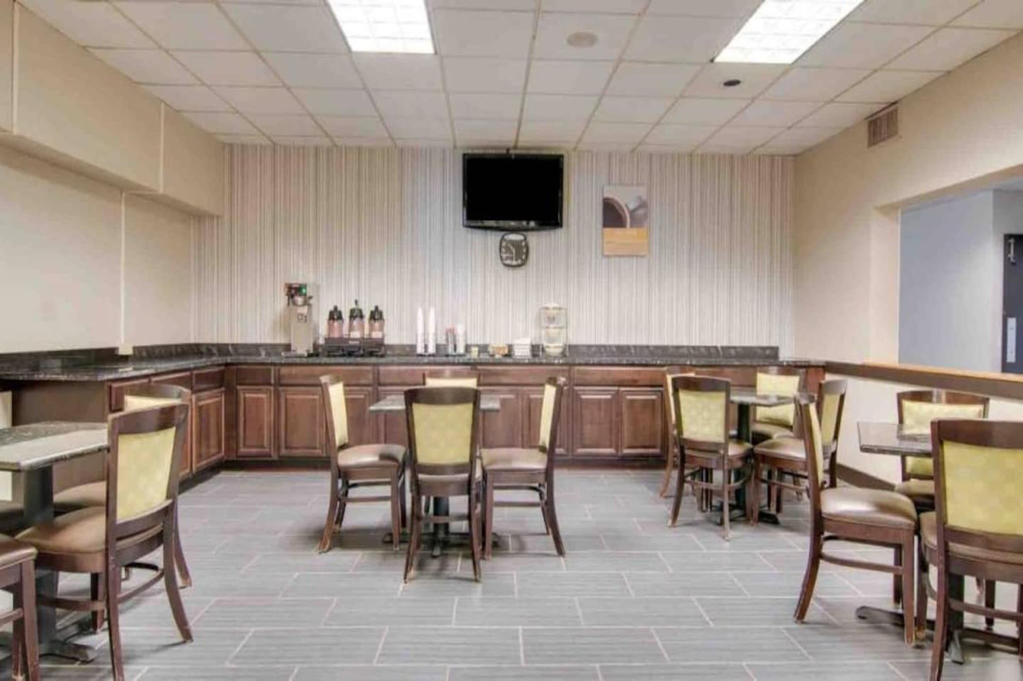 Habitaci ón de hotel con kitchenette, televisor de pantalla plana montado en la pared y comedor con mesas y sillas.