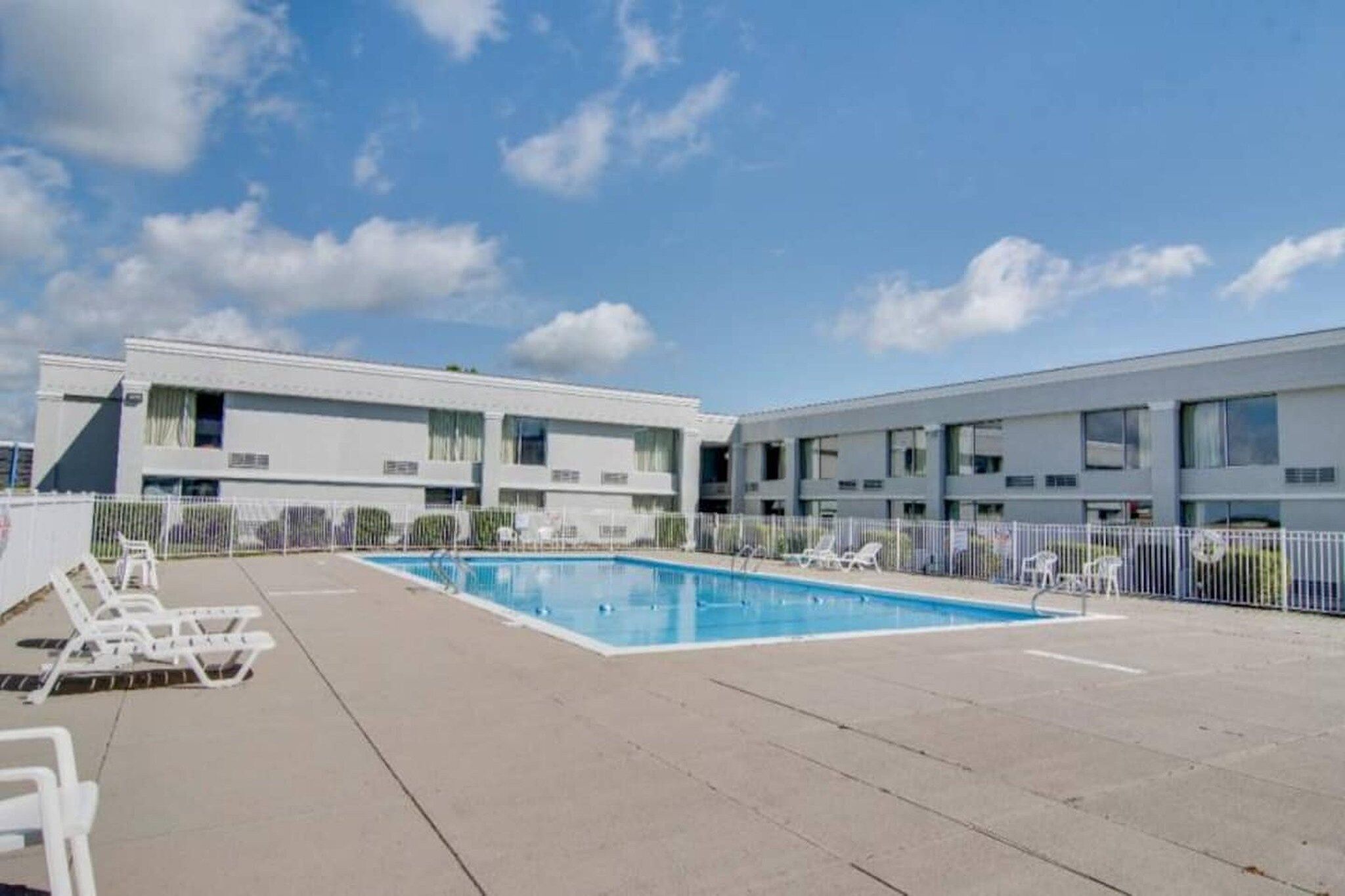 Un edificio moderno con piscina, sillas de descanso y cielo despejado.