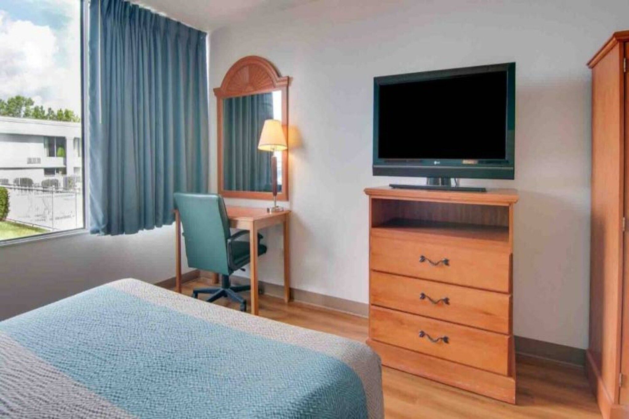 Ein Hotelzimmer mit einem Bett, einem Schreibtisch mit Stuhl, einem Fernseher und einem Kleiderschrank.