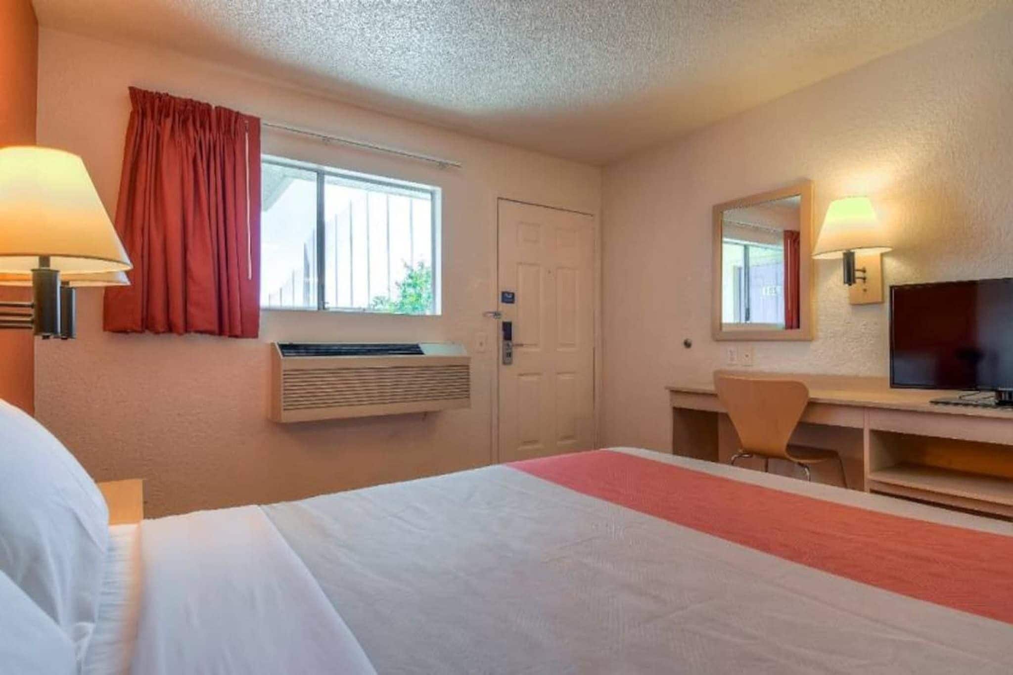 Ein Hotelzimmer mit einem Bett, einem Schreibtisch mit Stuhl, einem Fernseher und einem Fenster mit Vorhängen.