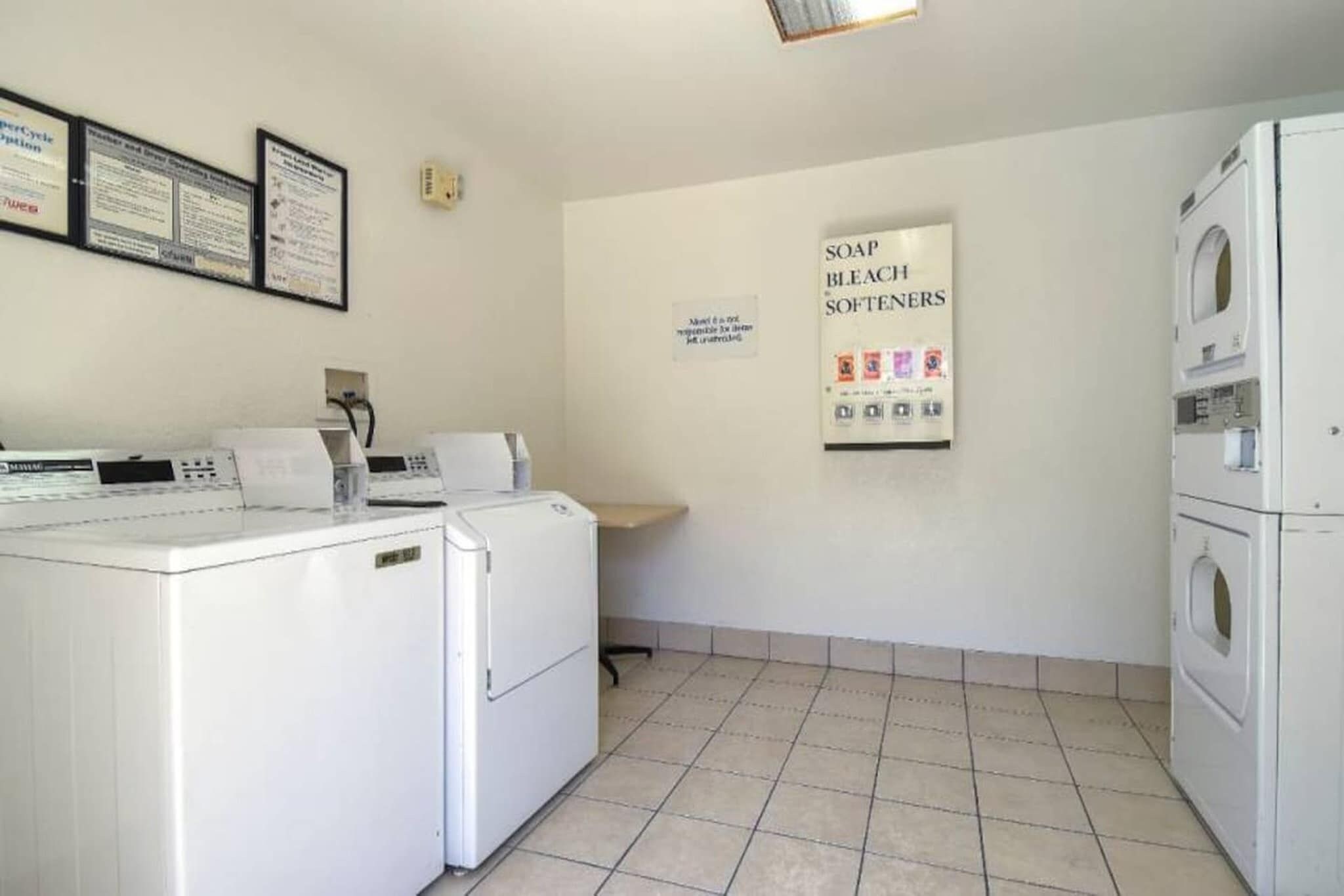 Una sala de bugaderia amb màquines de rentar i assecadores blanques, i un senyal que indica suavitzants, sabó i lleixiu.