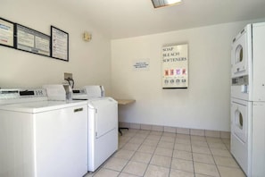 Una sala de bugaderia amb màquines de rentar i assecadores blanques, i un senyal que indica suavitzants, sabó i lleixiu.