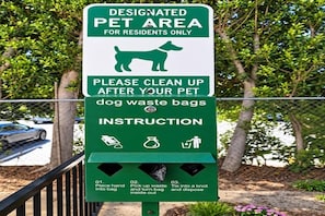 Señal con indicaciones para limpiar después de las mascotas, incluyendo zona designada para animales y disposición de bolsas para desechos.